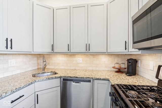 kitchen with backsplash, light stone countertops, stainless steel appliances, and a sink