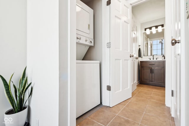 clothes washing area with laundry area, light tile patterned flooring, stacked washer and clothes dryer, and a sink