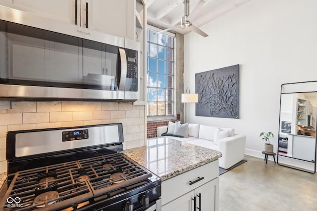 kitchen with light stone counters, finished concrete floors, decorative backsplash, appliances with stainless steel finishes, and beamed ceiling