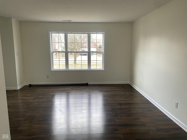 empty room with dark wood-type flooring, visible vents, and baseboards