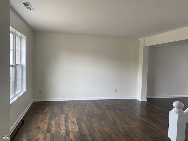 unfurnished room with dark wood-type flooring, decorative columns, visible vents, and baseboards