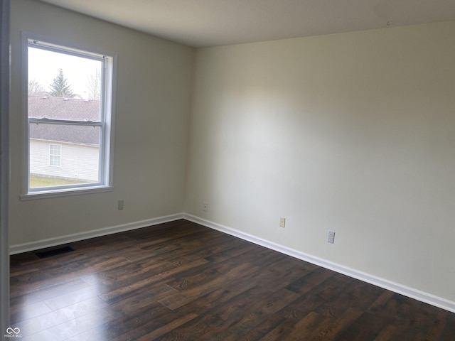 empty room featuring visible vents, dark wood-type flooring, a wealth of natural light, and baseboards