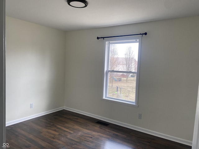 empty room featuring baseboards, dark wood-style flooring, visible vents, and a healthy amount of sunlight