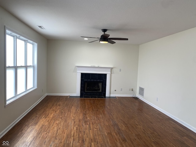 unfurnished living room featuring dark wood-style flooring, visible vents, a tiled fireplace, a ceiling fan, and baseboards