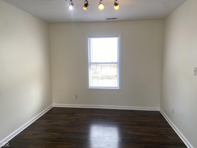 empty room featuring baseboards, visible vents, and dark wood finished floors