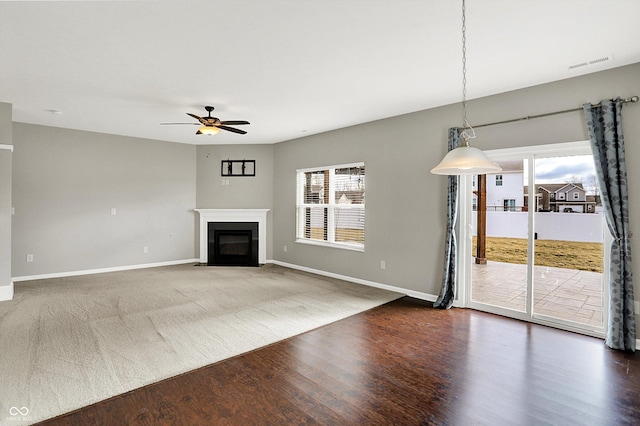 unfurnished living room featuring a fireplace with flush hearth, baseboards, ceiling fan, and wood finished floors