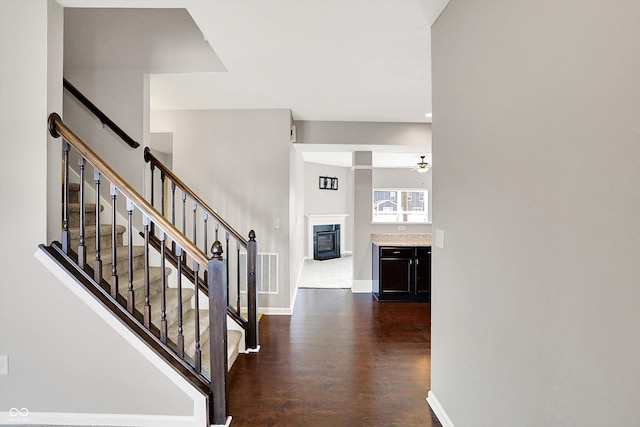 entryway featuring stairway, a ceiling fan, a glass covered fireplace, wood finished floors, and baseboards