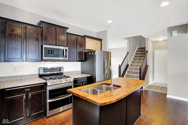 kitchen with butcher block countertops, a sink, appliances with stainless steel finishes, tasteful backsplash, and dark wood finished floors