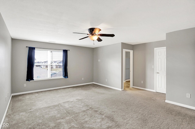 carpeted empty room with ceiling fan and baseboards