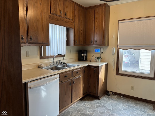 kitchen featuring stone finish floor, light countertops, dishwasher, and a sink