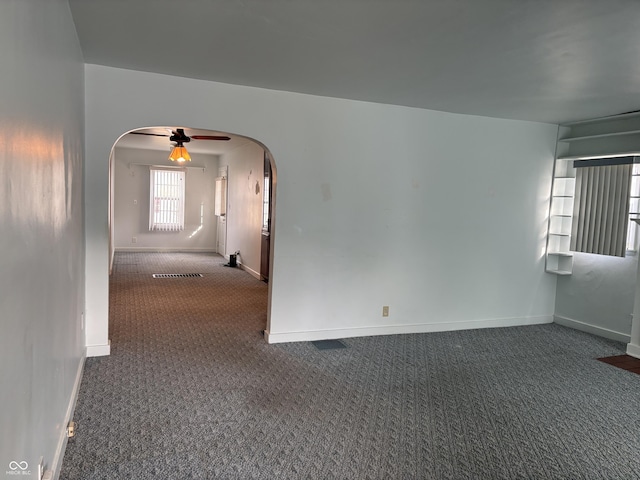 carpeted empty room featuring ceiling fan, visible vents, arched walkways, and baseboards