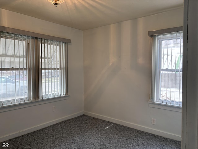 unfurnished room featuring plenty of natural light, dark carpet, and baseboards