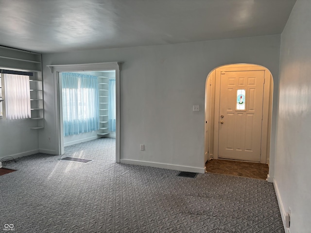 carpeted foyer with baseboards, visible vents, and arched walkways