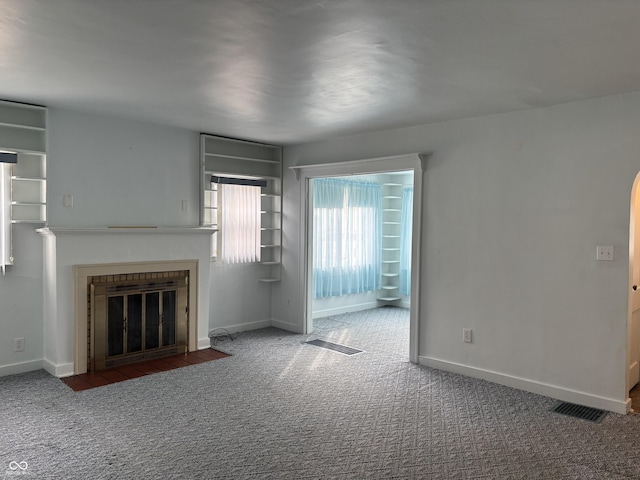 unfurnished living room featuring carpet floors, a fireplace with flush hearth, visible vents, and baseboards