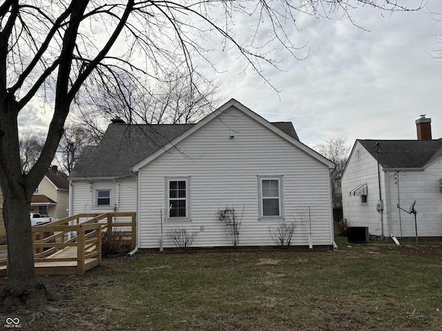 back of house featuring roof with shingles, a deck, and a yard