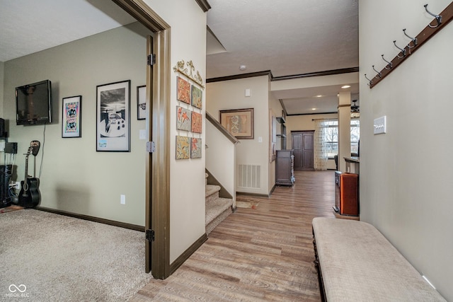 corridor with light wood finished floors, baseboards, visible vents, stairs, and crown molding