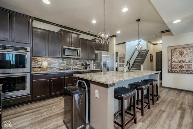 kitchen with stainless steel appliances, a sink, light stone countertops, and light wood-style floors