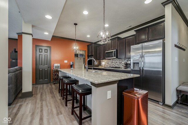 kitchen featuring decorative backsplash, appliances with stainless steel finishes, dark brown cabinets, light wood-style floors, and a sink