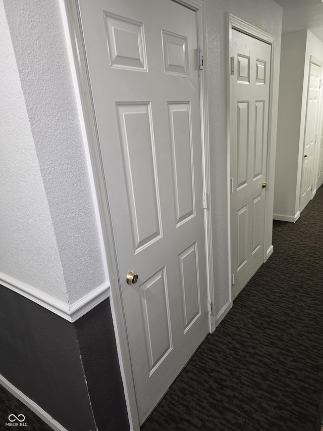 hallway with dark colored carpet and baseboards