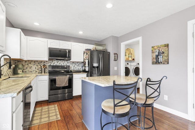 kitchen with washing machine and dryer, stainless steel appliances, a sink, decorative backsplash, and dark wood-style floors