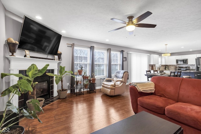 living room with a textured ceiling, baseboards, hardwood / wood-style floors, and a tiled fireplace