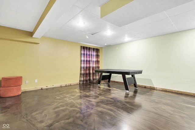 playroom with a paneled ceiling, concrete floors, and baseboards