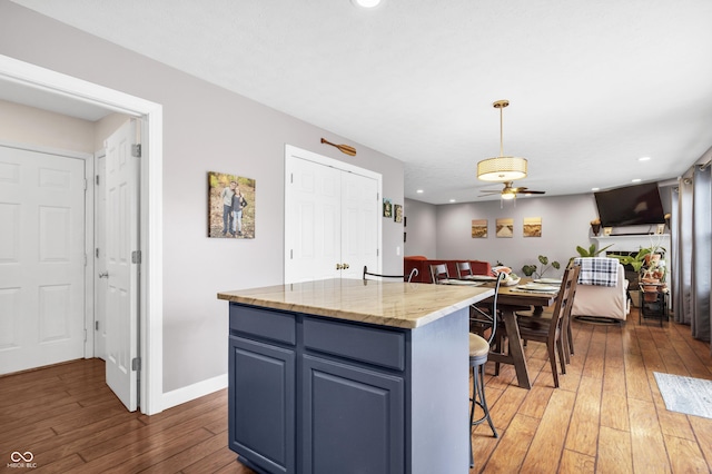 kitchen with baseboards, a breakfast bar area, a center island, blue cabinetry, and light wood-style floors