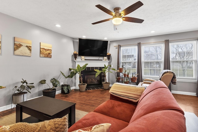 living room with a textured ceiling, a fireplace, baseboards, and wood finished floors