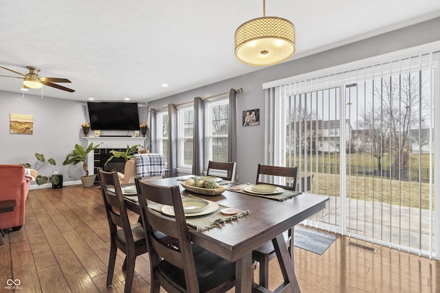 dining area with baseboards, visible vents, a tile fireplace, hardwood / wood-style flooring, and ceiling fan