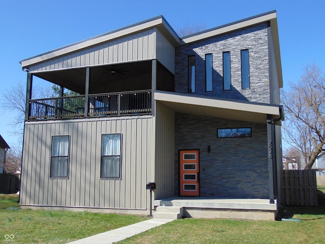 contemporary house featuring a front lawn, a balcony, and stone siding