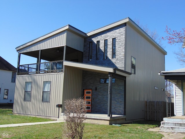 rear view of house featuring a balcony, a yard, and stone siding