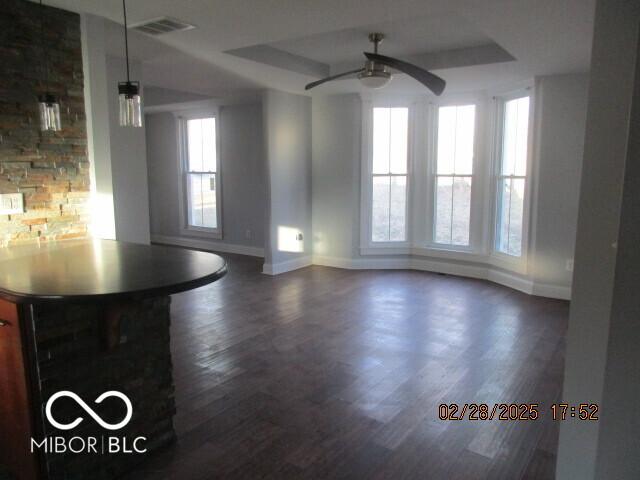 unfurnished dining area with dark wood-type flooring, a raised ceiling, visible vents, and a ceiling fan