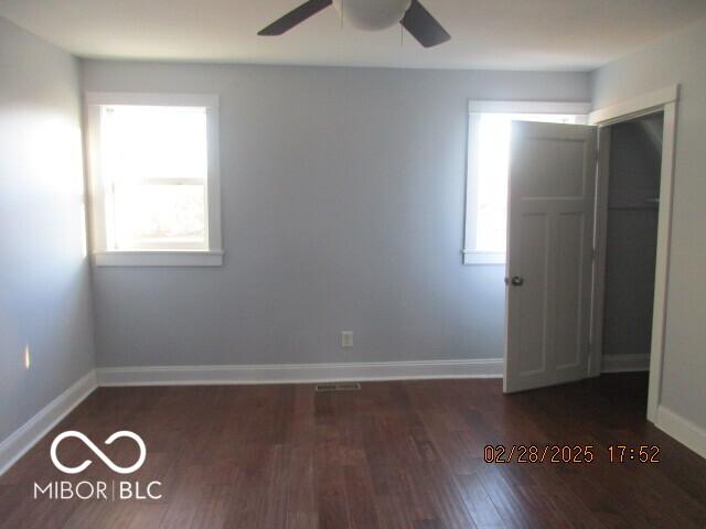 empty room featuring dark wood-type flooring, plenty of natural light, baseboards, and ceiling fan