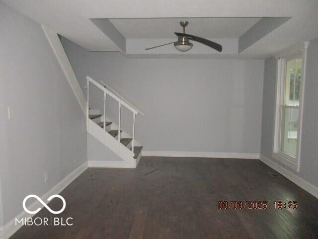 unfurnished room featuring a ceiling fan, a raised ceiling, baseboards, and stairs