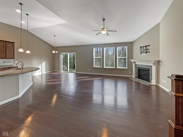 unfurnished living room featuring ceiling fan, a tile fireplace, a sink, vaulted ceiling, and dark wood finished floors