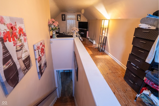 interior space with vaulted ceiling, a baseboard heating unit, wood-type flooring, and baseboards