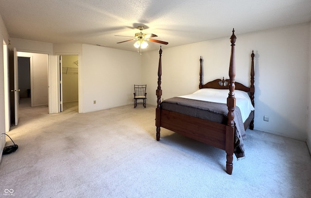 bedroom with ceiling fan, a walk in closet, a textured ceiling, and light colored carpet