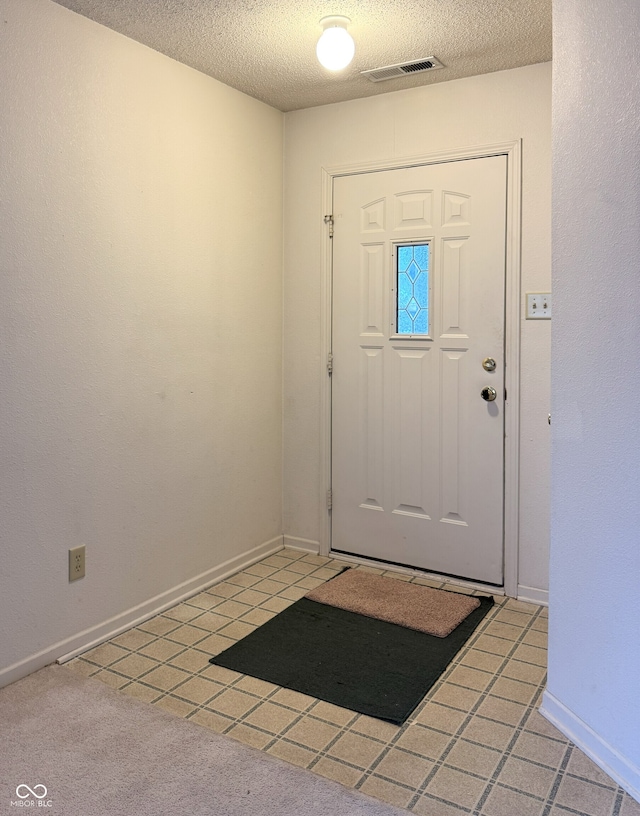 entryway with light tile patterned floors, baseboards, visible vents, and a textured ceiling