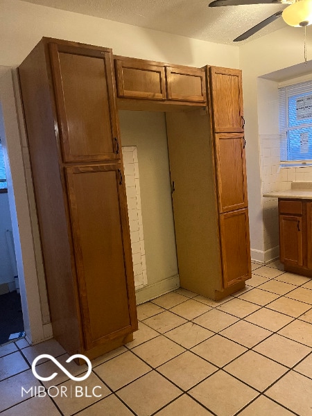 kitchen featuring brown cabinets, light tile patterned floors, backsplash, ceiling fan, and a textured ceiling