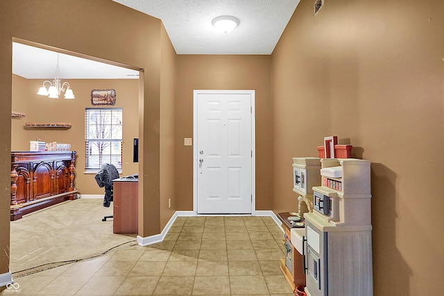 entryway with light tile patterned floors, baseboards, light colored carpet, a textured ceiling, and a notable chandelier