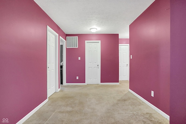 carpeted spare room featuring visible vents, a textured ceiling, and baseboards