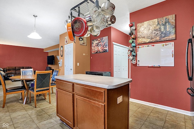 kitchen featuring decorative light fixtures, light countertops, brown cabinetry, a kitchen island, and baseboards