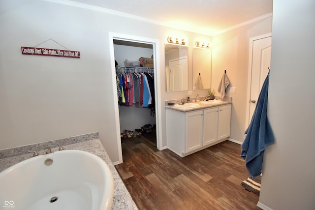 bathroom with a spacious closet, ornamental molding, vanity, wood finished floors, and a bath