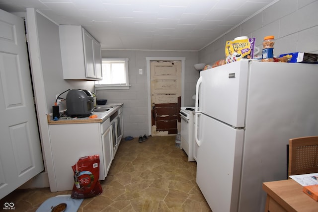 kitchen featuring light countertops, freestanding refrigerator, white cabinets, and concrete block wall