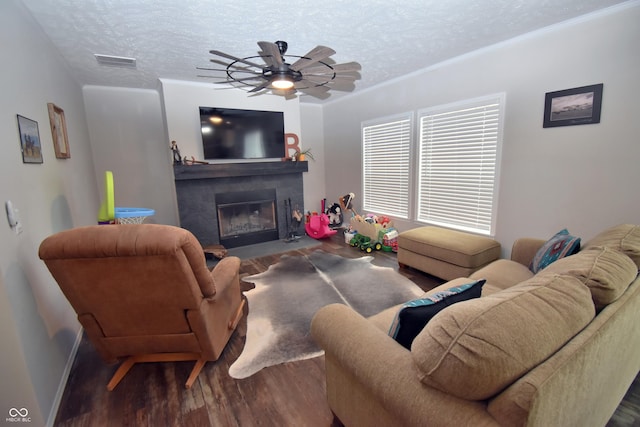 living room featuring a fireplace with flush hearth, visible vents, a textured ceiling, and wood finished floors