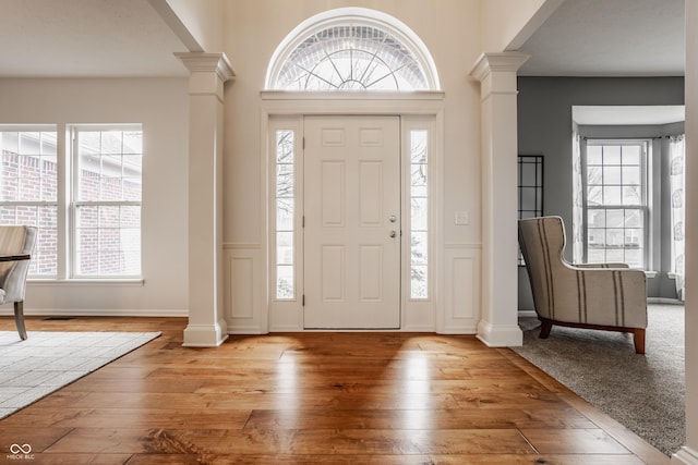 foyer with a healthy amount of sunlight, ornate columns, light wood-style flooring, and baseboards