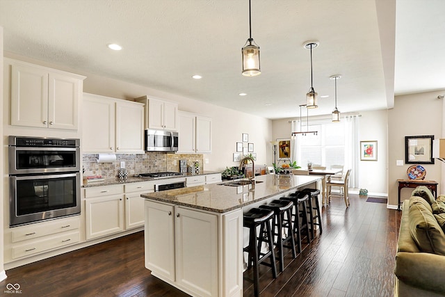 kitchen with a kitchen bar, a sink, tasteful backsplash, stainless steel appliances, and light stone countertops