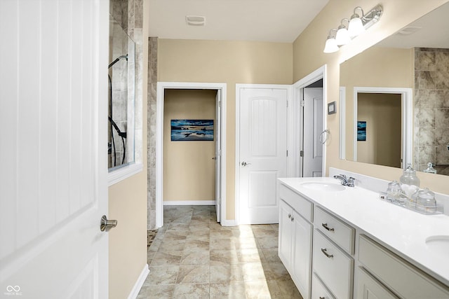 bathroom with a tile shower, double vanity, baseboards, and a sink