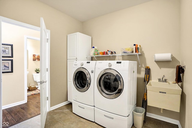 clothes washing area featuring cabinet space, washing machine and dryer, baseboards, and a sink