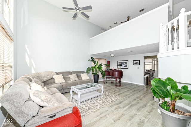 living area with ceiling fan, a high ceiling, baseboards, and wood finished floors